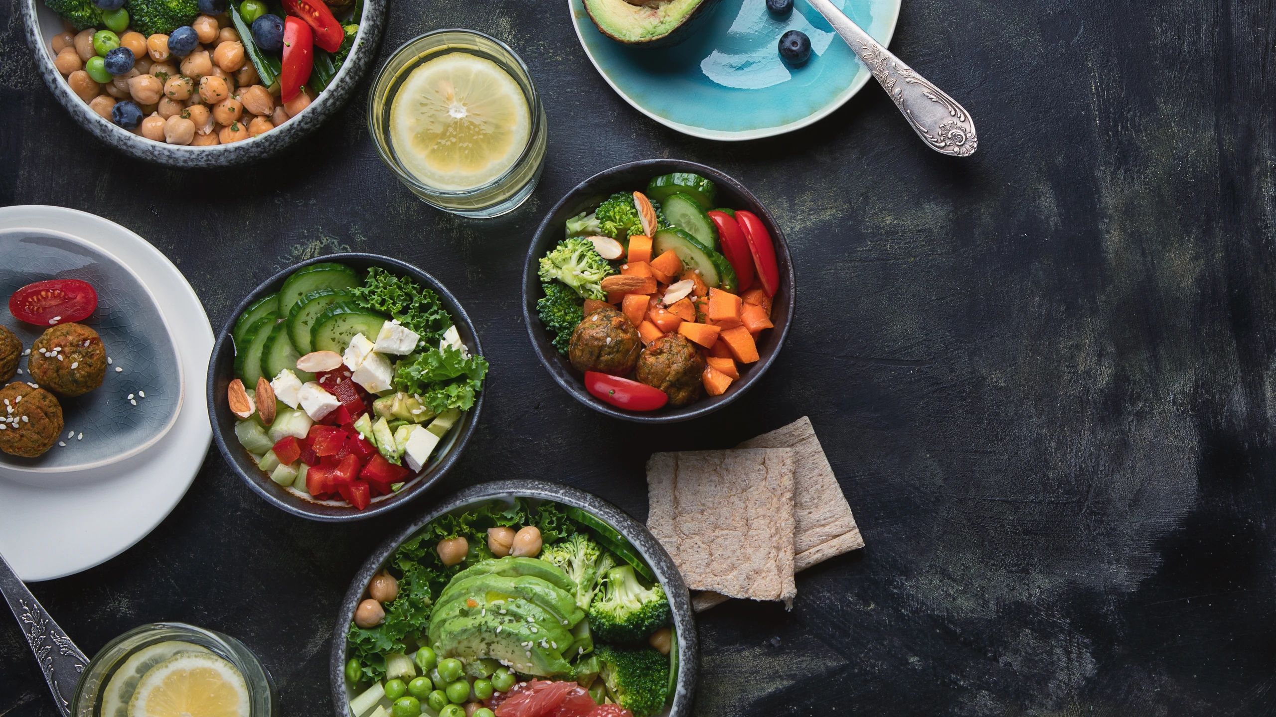 Bowls of vegetables, salad and lemon water on a charcoal table.
