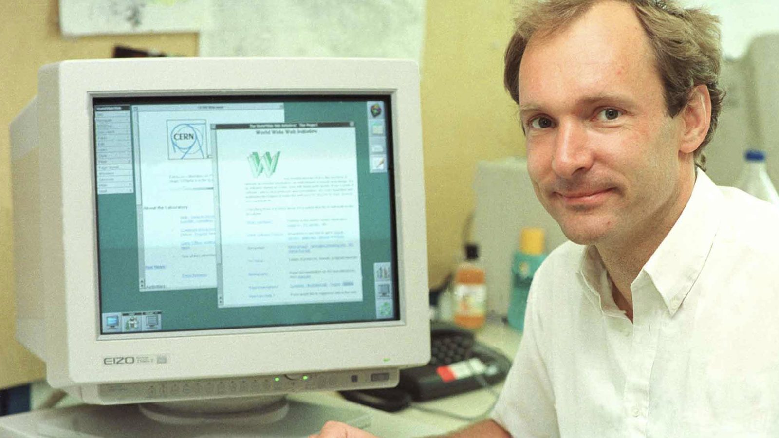 Tim Berners-Lee sitting beside a computer monitor showing an early World Wide Web page.