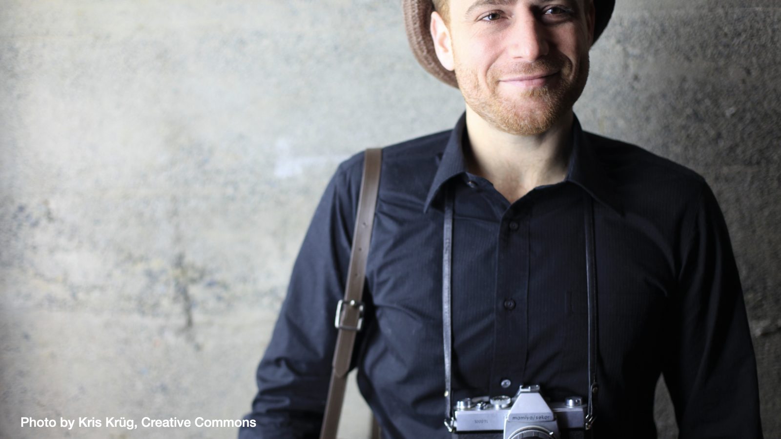 A photo of Stewart Butterfield wearing a hat and camera, credited to Kris Krüg.