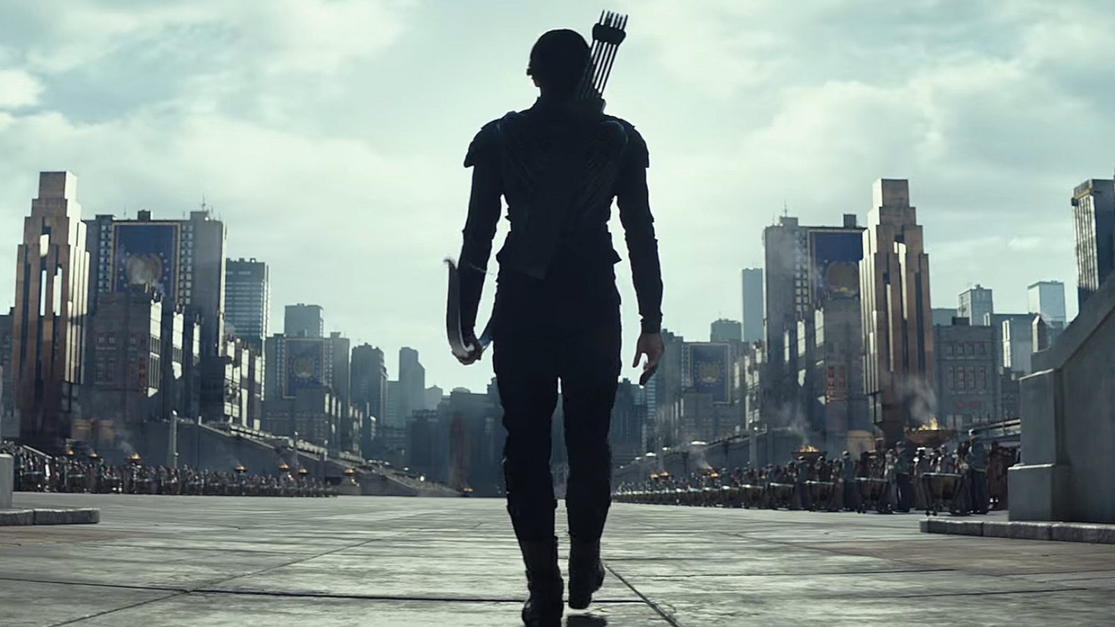 A silhouetted archer walks toward a crowd in a city scene from The Hunger Games.