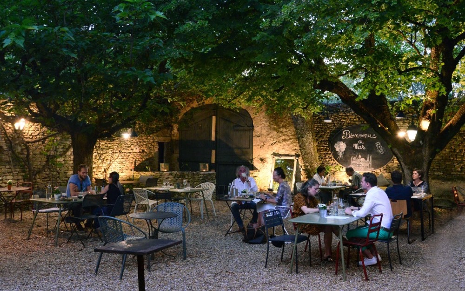 Diners beneath mature trees in Le Mas’s gravel courtyard in Les Imberts.