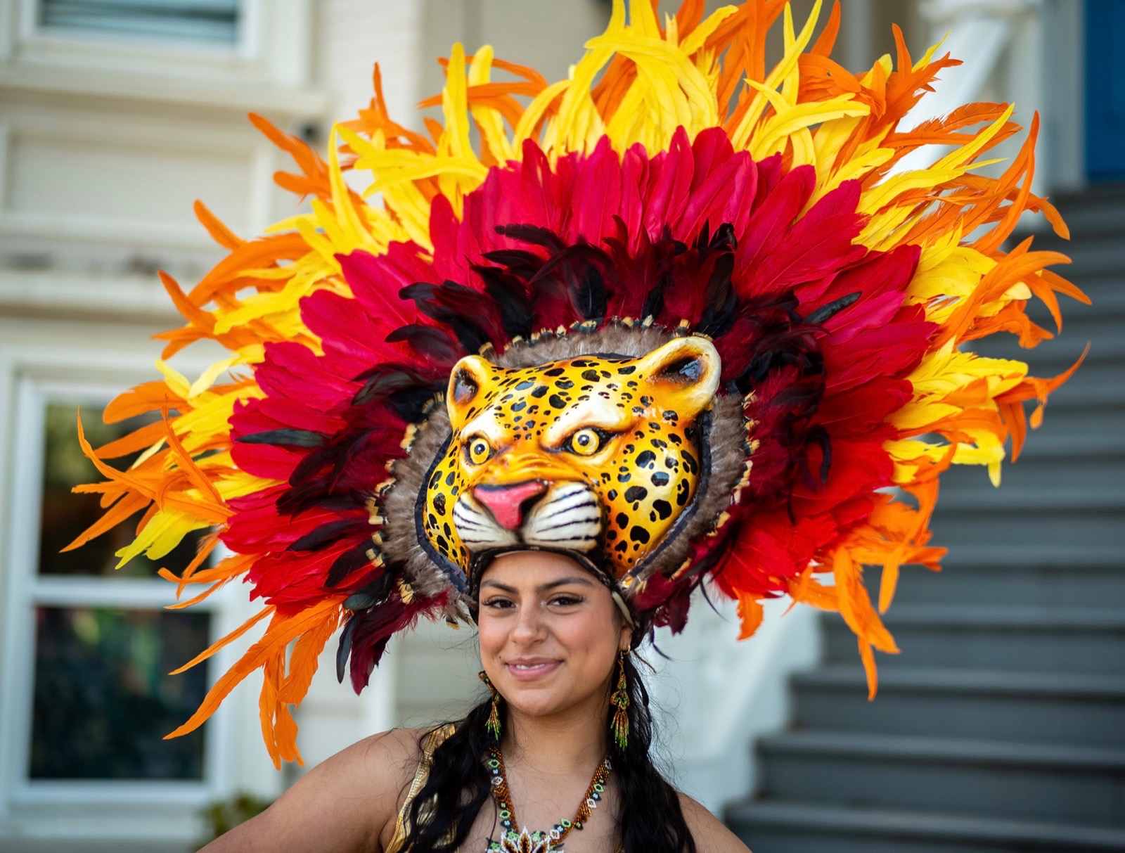 A person wearing a large spotted-cat headdress surrounded by red, orange and yellow feathers