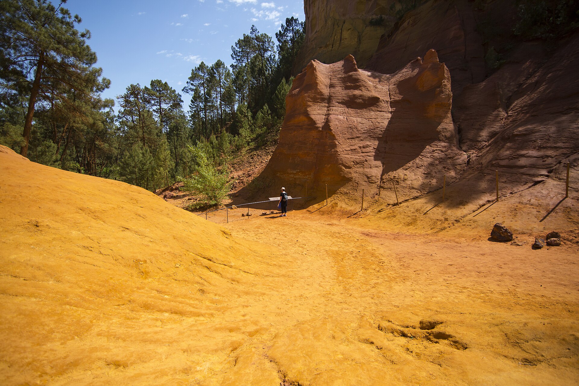 A path between golden earth, red ochre walls and green pine trees