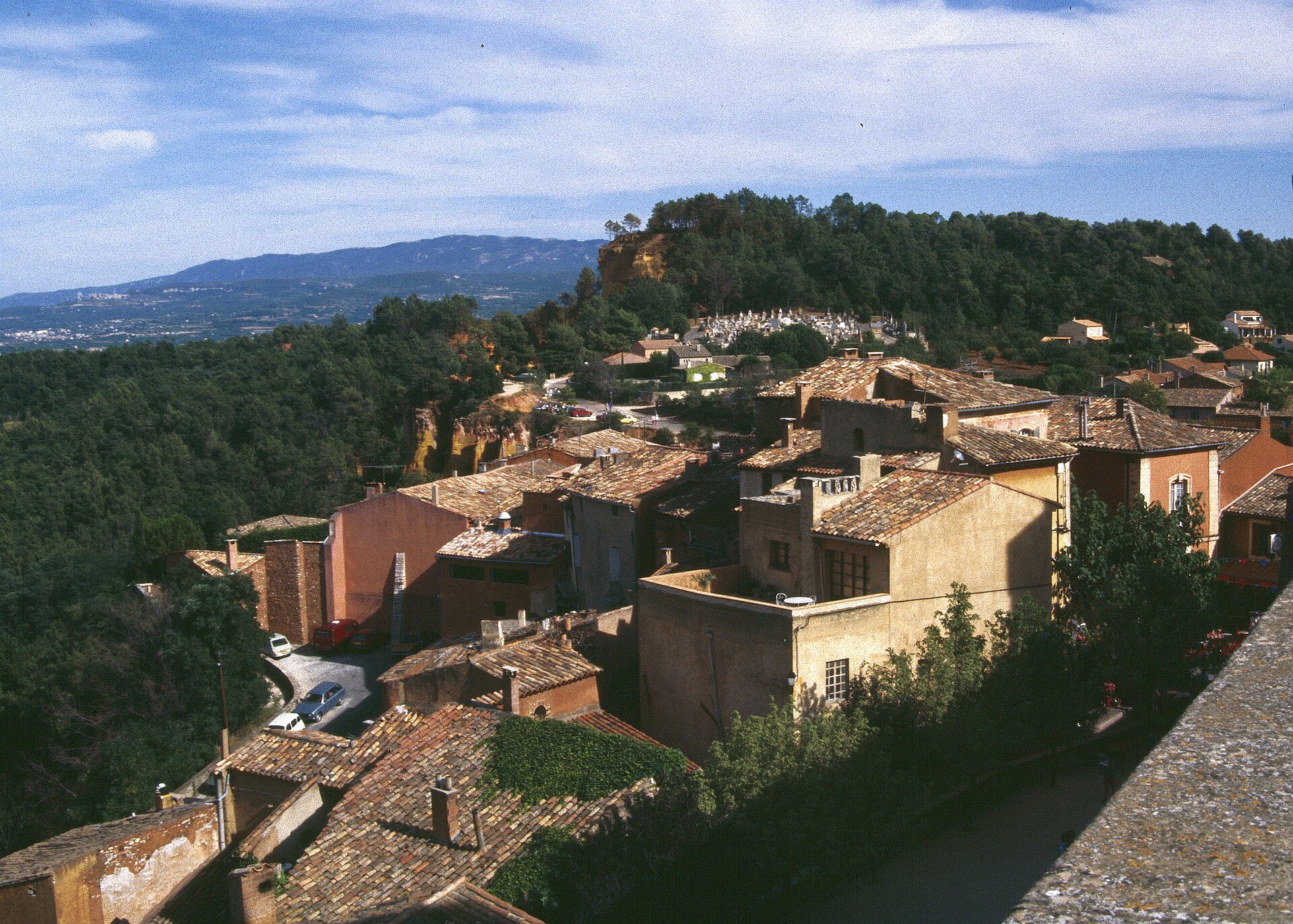 Terracotta rooftops, trees and the sculpted ochre ridge beyond Roussillon
