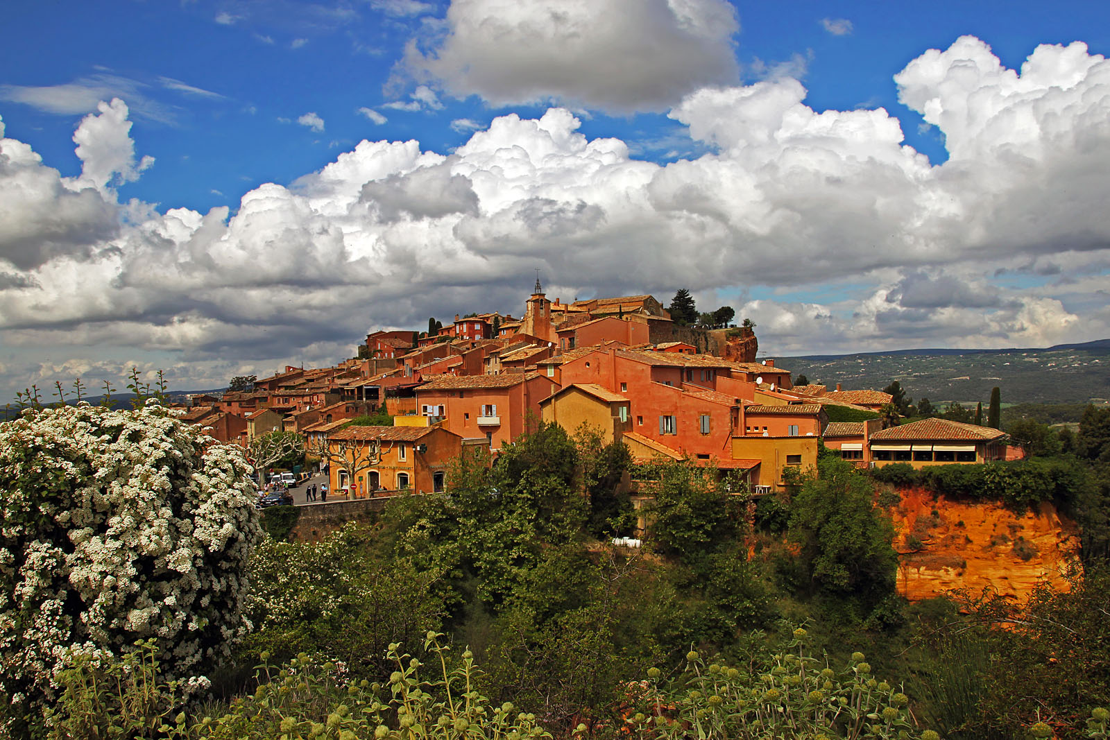 Roussillon glowing orange beneath a bank of bright summer clouds