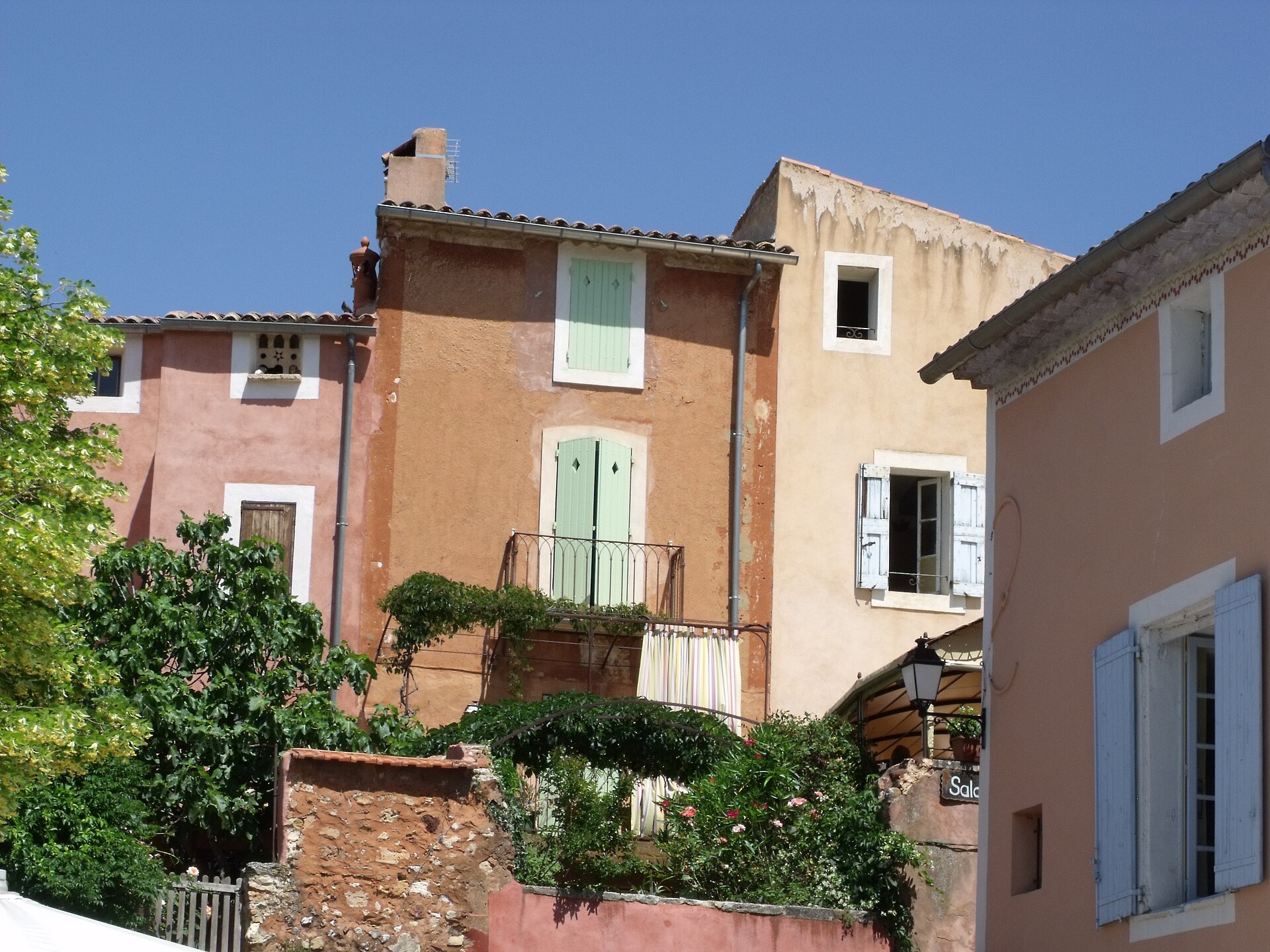 Pink and terracotta village façades with faded green shutters and plants